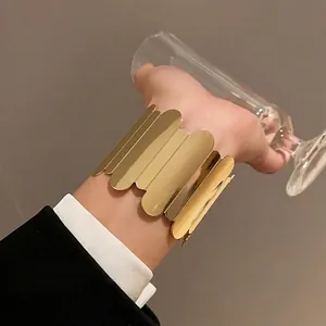 Elegant gold metallic open cuff bracelet with unique layered vertical leaf design on wrist.