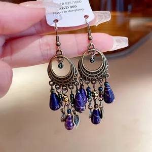 Dettaglio di orecchini etnici vintage con gocce marmorizzate viola e cerchi in bronzo.