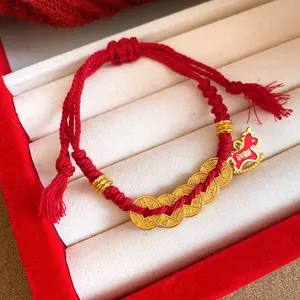 Detailed view of red braided rope bracelet with golden coins and horse pendant
