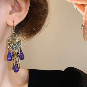 Dettaglio di orecchini etnici a goccia con perle viola e finiture in bronzo antico