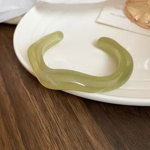 Gros plan d'un jonc en acrylique marbré vert au design ondulé sur une assiette blanche