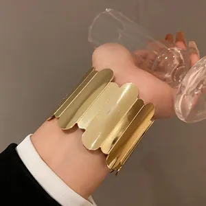 A detailed close-up showing a wide gold scalloped metal cuff bracelet on a woman's wrist