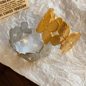 Detailed view of gold and silver metal butterfly open bracelets on textured paper.