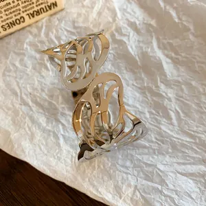 Detailed macro view of a silver hollowed leaf-patterned open cuff bracelet on white paper