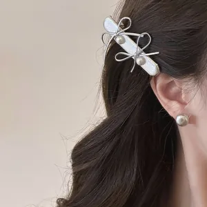 Close-up detail of a stylish silver bow hair clip with pearls worn on wavy dark hair.