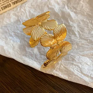 Detailed macro view of gold butterfly cuff bracelet with textured wings on white paper