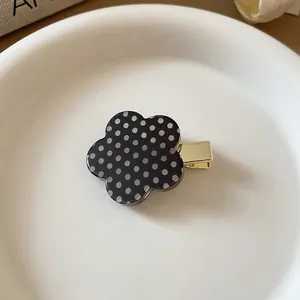 Detail view of a sweet black flower hair clip featuring white polka dots and a gold base