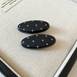 Detailed macro view of two elegant black oval hair clips with white polka dots on textured fabric
