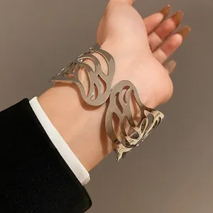Detailed view of a silver metallic open bangle featuring a hollow leaf design on a wrist.