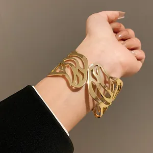 A detailed close-up shot of a golden metal leaf-shaped open cuff bracelet worn on a wrist.