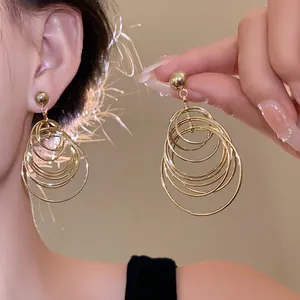 Detail view of gold layered geometric hoop drop earrings on model with warm lighting