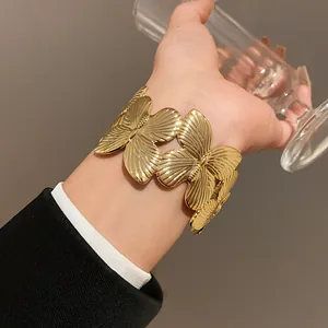 Close-up of a gold butterfly cuff bracelet worn on the wrist over a black suit sleeve