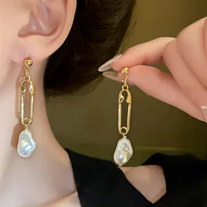 Detail of gold safety pin earrings with irregular pearl drops on ear and hand