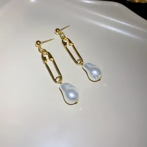 Detail view of elegant gold safety pin earrings with baroque pearls on a cream tray