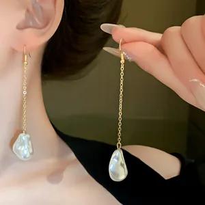 Close-up of French style baroque pearl tassel earrings shown on ear and held by hand.