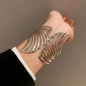 Macro detail of a silver metallic wing leaf open cuff bracelet worn on a stylish wrist.