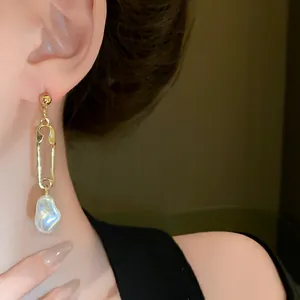 Close-up detail of a gold safety pin earring featuring a unique irregular white pearl.