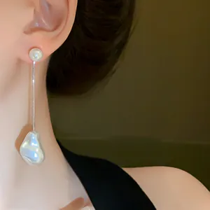Close-up of model wearing irregular baroque pearl drop earrings with snake chain.