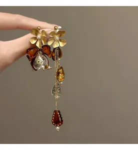 Close-up detail of asymmetrical flower bow earrings with amber resin beads and pearls