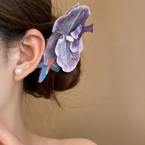Detailed view of a purple fabric orchid flower hair clip worn on a side hairstyle for women.