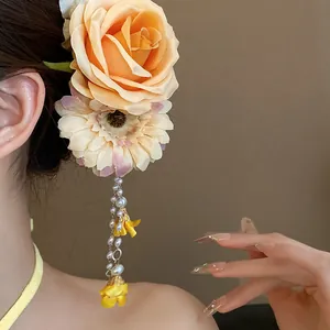 Detail view of a yellow fabric flower hair clip with pearl tassels worn by a model