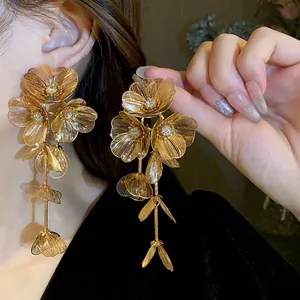 Detailed macro view of oversized golden flower tassel earrings worn on a fashion model