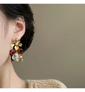Close-up of elegant asymmetric gold flower and amber bow earrings worn by a model
