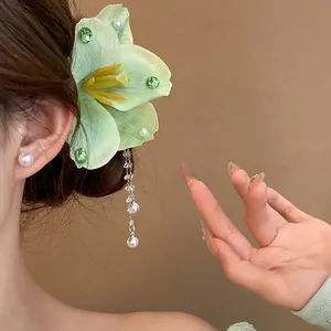 Close-up view of a light green fabric flower hair clip with an elegant pearl tassel on a model