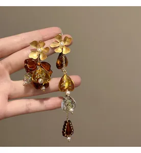 Detailed close-up of asymmetric flower bow earrings featuring amber resin heart-shaped charms.