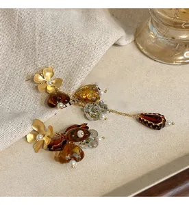 Close-up of asymmetric vintage gold flower earrings with amber glass beads and pearl accents.