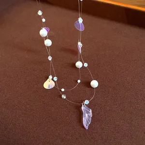 Close-up of shell sequins and fishtail pendant on a delicate pearl necklace for beach wear.