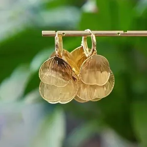 Dettaglio di orecchini a cerchio dorati con petali a cuore stratificati e texture a coste