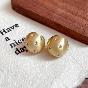 Close-up of matte gold round stud earrings with star-shaped crystal inlays