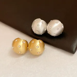 Detail view of brushed spherical stud earrings with star crystal inlays in gold and silver finish.