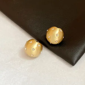 Detailed macro close-up of gold brushed round stud earrings with star-set stones