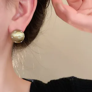 Close-up detail of a minimalist star-brushed gold round stud earring worn on a model's ear.
