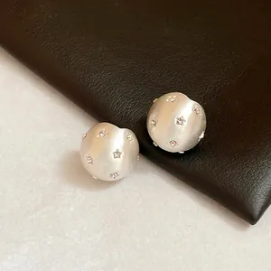 Close-up of brushed silver stud earrings featuring tiny star patterns with inset crystals