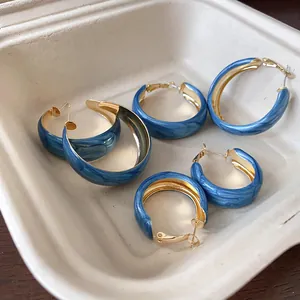Detailed macro view showing three sizes of Klein blue marbled hoop earrings on beige tray.