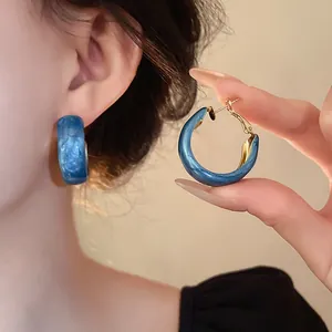 Close-up of Klein blue marbled hoop earrings worn on ear and held by hand