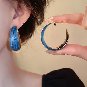 Close-up detail of Klein blue marbled C-shaped hoop earrings featuring a gold interior finish