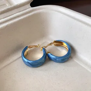 Close-up of Klein blue marbled hoop earrings with a glossy gold-tone finish.