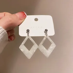 Primo piano di eleganti orecchini a rombo in resina marmorizzata bianca con perni in argento