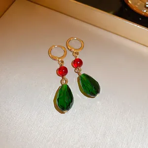 Primo piano di orecchini a goccia sfaccettati verdi con perline rosse e cerchi dorati