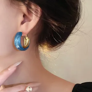 Detailed view of Klein blue marbled hoop earrings with a gold inner finish on a model