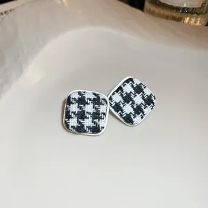 Dettaglio di orecchini a lobo in argento con motivo pied de poule bianco e nero classico.