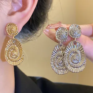 Elegant gold oval earrings with spiral texture shown worn on ear and held by hand.