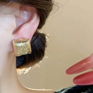 Détail de boucles d'oreilles clips géométriques dorées avec texture martelée unique