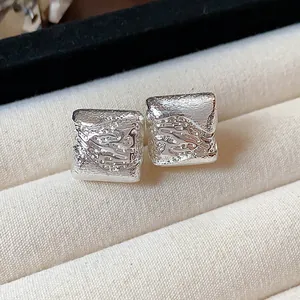 Détail de boucles d'oreilles géométriques en argent avec une surface texturée.