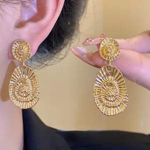 Macro detail of elegant gold oval earrings featuring an intricate spiral textured pattern