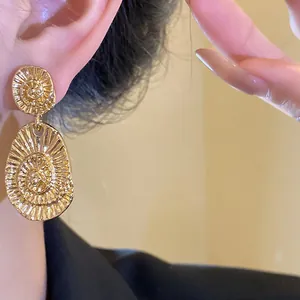 Close-up macro shot of elegant gold oval textured drop earring worn on ear with shine.